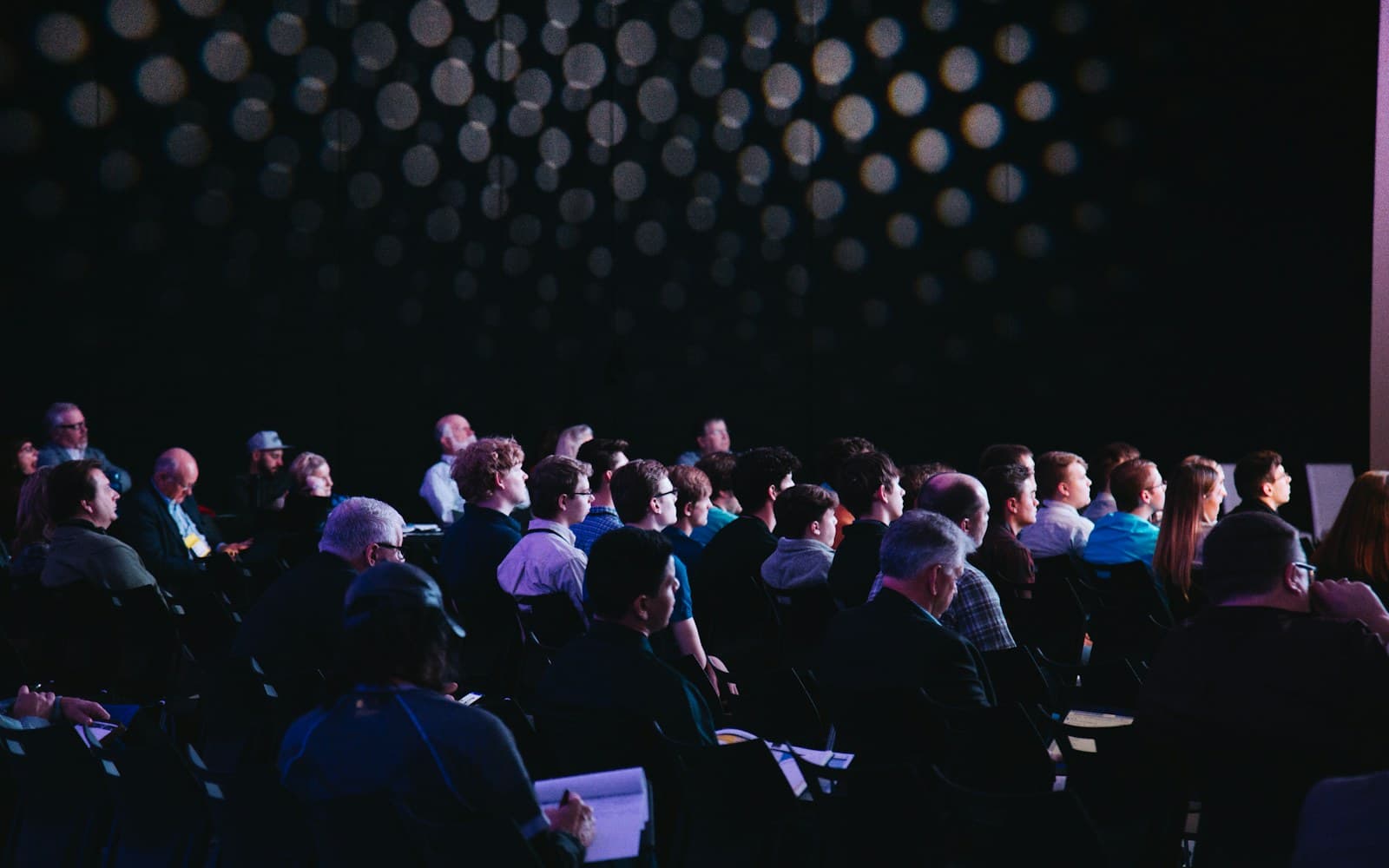Conference audience facing a stage under rows of lights